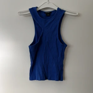 Blå ribbad linnetopp från Monki - Säljer en snygg blå ribbad linnetopp från Monki. Den är ärmlös och har en tight passform, perfekt för sommardagar eller som ett lager under en jacka. Toppen är i storlek S och är i nyskick.