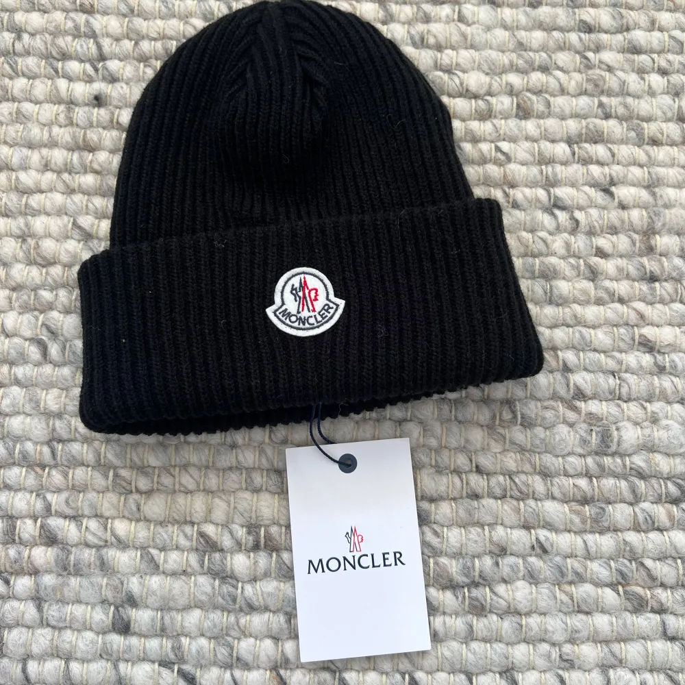 Säljer en snygg svart stickad mössa från Moncler. Den har en klassisk design med Monclers logga broderad framtill. Perfekt för att hålla sig varm och stilren under kalla dagar.. Accessoarer.