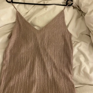 Glittrig fest topp från Gina Tricot - Säljer en snygg glittrig fest topp från Gina Tricot i en ljus rosa ton. Toppen har smala axelband och en v-ringad design. Perfekt för en kväll ute eller en speciell tillställning. ✨