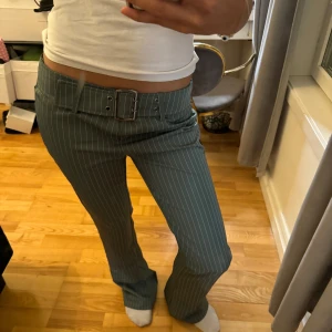 kostymbyxor med bälte - Snygga gröna kostymbyxor med vita ränder och ett matchande bälte. Byxorna har en lågmidjad passform och vida ben, vilket ger en trendig look. Perfekta för en stilren outfit. Det är en fläck på ena låret, men den borde gå bort. Säljer för de inte kommer till användning!