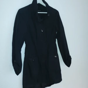 Svart jacka från Vero Moda - Snygg svart jacka från Vero Moda med knappar och hög krage. Jackan har långa ärmar och en stilren design som passar perfekt för kyligare dagar. Den är tillverkad i ett lätt material och har praktiska fickor med knappar.