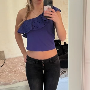 Blå oneshoulder topp - Säljer en snygg blå oneshoulder topp med volangdetaljer. Toppen är croppad och perfekt för sommarens varma dagar. Den har ett stilrent och modernt utseende som passar till många olika outfits.