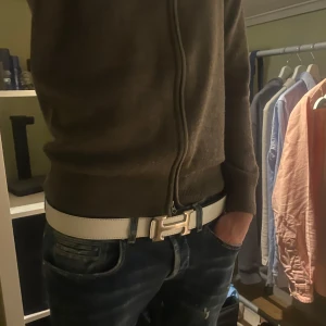 Vitt bälte med silverfärgat spänne - Snyggt vitt bälte med ett stilrent silverfärgat spänne. Perfekt för att ge en fräsch touch till din outfit. Bältet är tillverkat i ett material som liknar skinn och har en klassisk design.