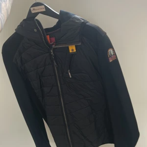 Svart jacka från Parajumpers - Snygg svart jacka från Parajumpers med quiltad design och dragkedja framtill. Jackan har en huva och en liten bröstficka med dragkedja. Perfekt för kyligare dagar.