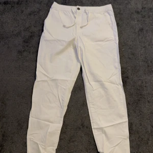 Vita byxor med snörning - Snygga finare vita linnebyxor med elastisk midja och snörning framtill. Perfekta för en avslappnad stil. Byxorna har en rak passform och är tillverkade i ett lätt material.