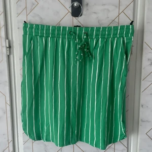 Nyköpt randiga kjol - Nyköpt grön kjol med vita ränder i super mjukt och stretchiga material. En elastisk midja med snörning för justerbar passform. Perfekta för en avslappnad stil.