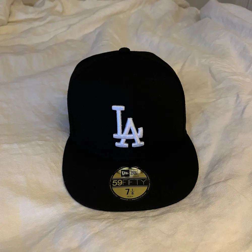 Snygg svart keps från New Era med LA-logga broderad i vitt framtill. Kepsen har en klassisk 59FIFTY design och är tillverkad i 100% polyester. Perfekt för att komplettera din stil med en sportig touch.. Asusteet.