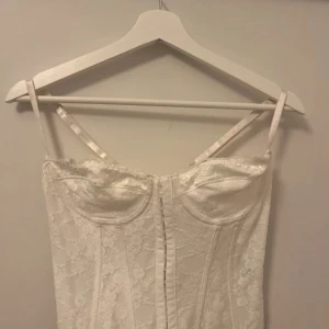 Vit spetskorsett med snörning - Elegant vit korsett i spets med smala axelband och snörning i ryggen. Perfekt för en stilfull look.