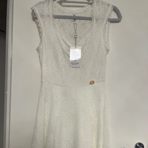 Vit spetsklänning från Chi Chi London - Elegant vit spetsklänning från Chi Chi London med vacker spetsdetaljering. Klänningen har en ärmlös design och en klassisk rund halsringning. Perfekt för sommarens festligheter eller en romantisk middag. 💫