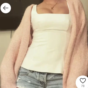 Lindex kofta - Säljer en stilren vit korsettliknande topp med fyrkantig urringning. Perfekt för att matcha med jeans eller kjol för en chic look. Toppen har en figurnära passform som framhäver silhuetten.