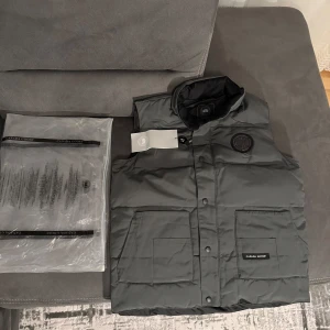 Canada Goose väst - Säljer en stilren svart dunväst från Canada Goose. Västen har en broderad logotyp på bröstet och praktiska fickor framtill. Perfekt för kyligare dagar med sin quiltade design.