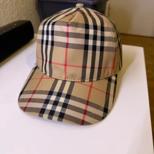 Burberry Keps - Snygg keps från Burberry med klassiskt rutigt mönster i beige, svart och rött. Kepsen har justerbar passform baktill och en broderad logotyp. Perfekt för en stilren look.