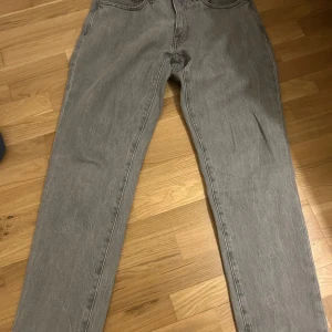 Grå jeansbyxor - Snygga grå jeansbyxor med en klassisk femficksdesign. De har en rak passform och är perfekta för en avslappnad stil. Byxorna har en knapp och dragkedja framtill.