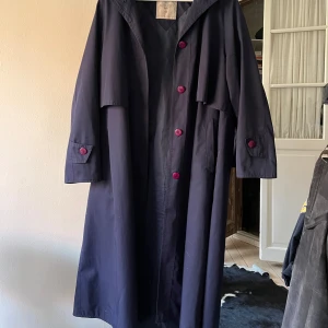 Mörkblå kappa från Aquabury - Säljer en elegant mörkblå kappa från Aquabury med knappar i rosa färg. Klassisk design med långa ärmar och en stilren krage.