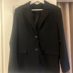 Svart kavaj från NA-KD - Elegant svart kavaj från NA-KD med två knappar framtill och klassiska slag. Perfekt för en stilren look. Tillverkad i ett mjukt material som ger en bekväm passform.