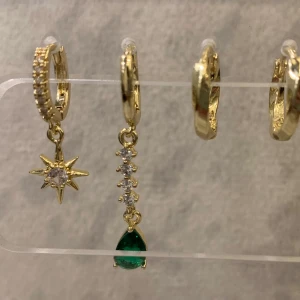 Guldplatsenärat  örhängen med stjärna och grön sten - Säljer ett set med fyra guldörhängen. Två av dem har hängande detaljer: en med en stjärna och en klar sten, och en med en rad av små stenar och en grön droppe. Perfekt för att mixa och matcha!