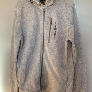 Grå huvtröja från Sail Racing - Snygg grå huvtröja från Sail Racing i storlek 160. En  justerbar huva med snörning.  Perfekt till vår och höst. Nypris 1000kr men säljer för 600kr pga defekten på bild 5 den är på båda ärmanarna men halva. Defekten är knappast synlig. 💞