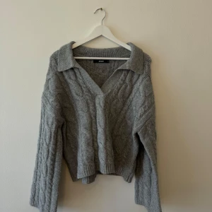 Grå stickad tröja från Bik Bok - Säljer en supermysig grå stickad tröja från Bik Bok. Den har en snygg kabelstickad design och en v-ringad krage som ger en stilren look. Perfekt för höst och vinter när du vill hålla dig varm och trendig. Tröjan har långa ärmar och en normal passform. Perfekt för både vardag och mysiga hemmakvällar!