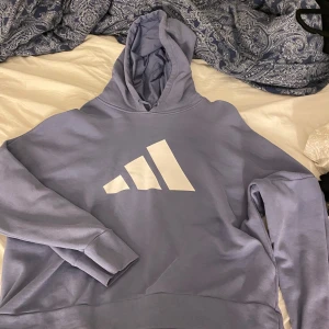 Ljusblå hoodie från Adidas - Säljer en snygg ljusblå hoodie från Adidas. Den är supermjuk och perfekt för både chill och träning. Hoodien har en stor vit Adidas-logga på framsidan och en bekväm passform. Den är i bra skick och redo för nya äventyr!
