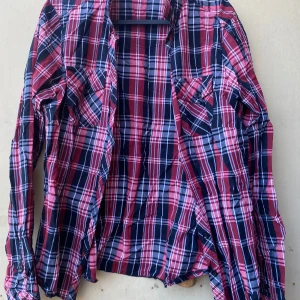 Rutig skjorta från Lindex - Säljer en supercool rutig skjorta från Lindex i rött, blått och vitt. Skjortan har långa ärmar och en klassisk krage. Perfekt för en avslappnad stil eller en dag på stan. Den är i bra skick och redo för nya äventyr!