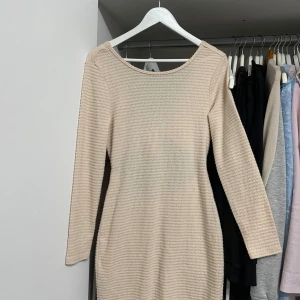 Beige stickad klänning med knyt - Säljer en superfin beige stickad klänning med långärmad design. Den har en snygg knytning framtill som ger en extra detalj. Perfekt för höst och vinter, och den är både mysig och stilren. Passar perfekt till både vardag och fest! Aldrig använd heller