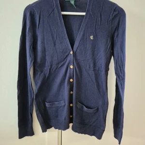 Kofta Ralph Lauren - Marinblå kofta med guld färgad märke och knappat från Ralph Lauren. Fickor på framsidan. Tunn och stechbar. Mjuk material. Använd några gånger. Storlek XS. 100% bomull. Lite nopprig.