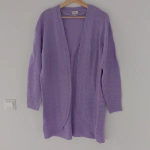 Ljuslila stickad kofta från Kaffe - Säljer en superfin ljuslila stickad kofta från Kaffe. Den är perfekt för både vår och höst med sin mysiga och mjuka känsla. Koftan har långa ärmar och en öppen design utan knappar, vilket gör den lätt att slänga på sig över vilken outfit som helst. Perfekt för att hålla sig varm och stilren!