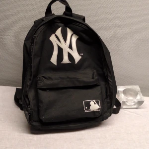 Old school Svart NY baseball ryggsäck med MLB och New York yankies loggor. - Snygg svart ryggsäck med New York Yankees-logga och Major League Baseball-märke. Perfekt för sportiga tillfällen eller vardagsbruk. Ryggsäcken har justerbara axelremmar och en praktisk ytterficka med dragkedja.