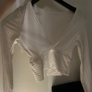 Vit ribbad omlottopp - Vit ribbad omlottopp med långa ärmar. Toppen har en omlottdesign som ger en smickrande passform. Ganska V-ringad.