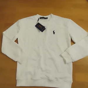 Vit tröja från Ralph Lauren - Säljer en stilren vit tröja från Ralph Lauren med det klassiska broderade logotypen på bröstet. Tröjan har långa ärmar och en bekväm passform. Perfekt för en avslappnad och snygg look. Priset kan diskuteras vid snabb affär!