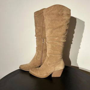 Beige mockastövlar med klack - Snygga beige stövlar i mocka med en bekväm klack och dragkedja på sidan. Perfekta för höst och vinter. Endast andvämt 2 ggr. 