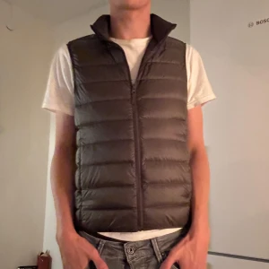 Olivgrön dunväst från Uniqlo - Säljer en stilren svart dunväst från Uniqlo. Västen är ultralätt och har en praktisk dragkedja framtill. Perfekt för lager-på-lager under kyliga dagar.