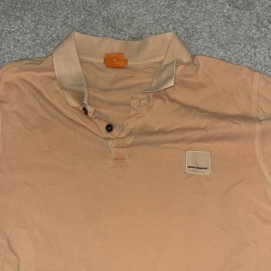 Beige pikétröja från Boss Orange - Säljer en stilren beige pikétröja från Boss Orange. Tröjan har en klassisk krage med knappar och en diskret logotyp på bröstet. Perfekt för en avslappnad men ändå snygg look.