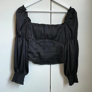 Svart offshoulder topp - Snygg svart offshoulder topp med långa puffärmar och smockdetaljer på baksidan. Perfekt för en stilren look.
