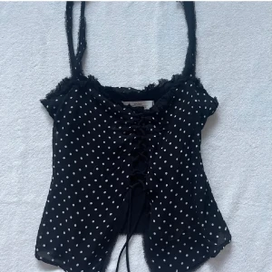 Svart prickig topp från Zara - Snygg svart prickig topp från Zara med smala axelband och snörning framtill. Bilderna är lånade
