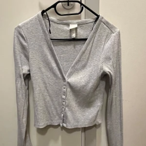 Grå ribbad kofta - Säljer en stilren grå ribbad kofta med v-ringning och knappar framtill. Nästan aldrig använd så tröjan är i fint skick