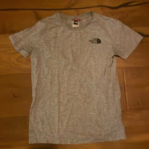 Grå t-shirt från The North Face - Snygg grå t-shirt från The North Face med tryck på bröstet och ryggen. Perfekt för en avslappnad stil. Tillverkad i mjukt material för extra komfort.