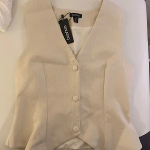 Beige topp väst från Boohoo - Snygg beige topp väst från Boohoo med knappar framtill och v-ringad design. Helt ny med prislapp kvar. 