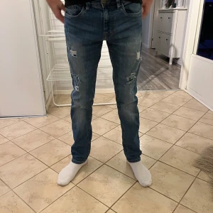 Blå jeans med slitningar - Snygga blå jeans med slitningar på låren och knäna. De har en klassisk femficksdesign och en normal passform. Perfekta för en avslappnad stil.