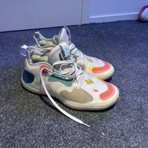 basketskor med snörning - Säljer ett par unika sneakers med en färgglad design i vitt, blått, grönt, gult och rosa. Skorna har snörning och en bekväm sula med färgglada detaljer. Perfekta för dig som vill sticka ut!