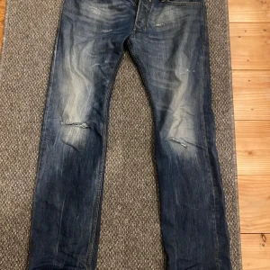 Blå jeans från Diesel - Säljer ett par snygga blå jeans från Diesel med en klassisk femficksdesign. Jeansen har en lätt slitning på framsidan och en bekväm passform. Perfekta för en avslappnad stil.