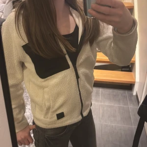 Vit teddyjacka med luva - Mysig vit fleecejacka med luva och dragkedja. Jackan har en svart bröstficka och svarta detaljer.Säljer då den har blivit för liten❤️