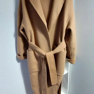Kamelfärgad kappa med bälte Zara XS - Snygg kamelfärgad kappa med bälte i midjan för en stilren look. Den har långa ärmar och en klassisk design som passar perfekt för kyligare dagar. Perfekt för att hålla stilen i höst och vinter. Från Zara strl XS men passar även S