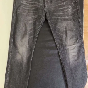 Grå jeans från Emporio Armani - Snygga grå jeans från Emporio Armani med en cool slitningseffekt. De har en klassisk femficksdesign och en knappgylf. Perfekta för en stilren look.