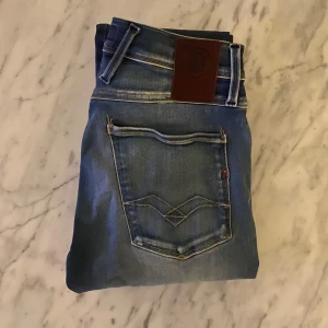Replay anbass hyperflex - Snygga blå jeans från Replay med slitna detaljer och en klassisk femficksdesign. De har en knappgylf och är tillverkade i ett stretchigt material för extra komfort. Perfekta för en avslappnad stil.