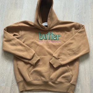 Brun hoodie från Butter - Säljer en snygg brun hoodie från Butter med broderad text i grön och lila på framsidan. Riktigt bra kvalitet, muddarna vid midjan gör sin funktion så den blir lite cropped. Storlek M men kanske lite större i storleken eftersom att den är oversized så hade passat L också. Tveka inte vid frågor! Pris kan vara diskuterbart 