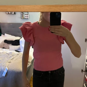 Rosa ribbad topp från Zara - Säljer en söt rosa ribbad topp från Zara med volangdetaljer på axlarna. Perfekt för att ge en färgklick till din outfit. Toppen har en normal passform och är ärmlös.