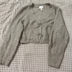 Grå stickad kofta - Säljer en mysig grå stickad kofta med v-ringning och knytband framtill. Koftan är croppad och har långa ärmar, perfekt för lager på lager-stil. Passar utmärkt till både vardag och lite finare tillfällen. Om ni vill se den på, skriv gärna!