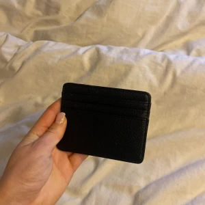 Svart plånbok i skinn - Säljer en stilren svart plånbok i skinn med flera kortfack. Perfekt för att hålla dina kort organiserade och lättillgängliga. Enkel och smidig design som passar i fickan.