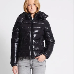 Svart pufferjacka från 157 - Snygg svart pufferjacka från 157 med glansig finish. Jackan har en dragkedja framtill och en hög krage för extra värme. Perfekt för kyliga dagar.